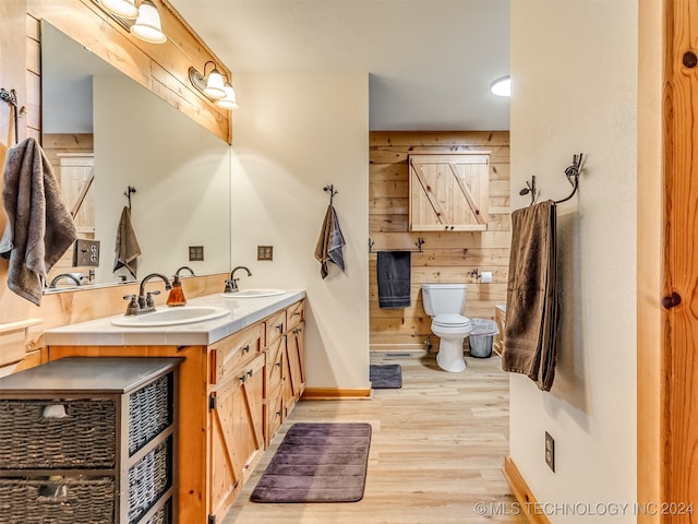 bathroom featuring hardwood / wood-style floors, wooden walls, toilet, and vanity