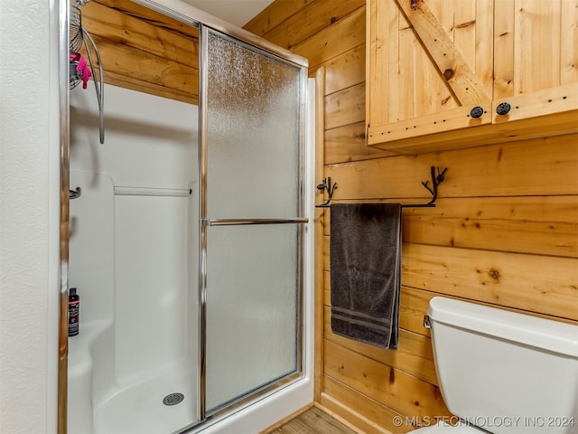 full bathroom featuring a shower stall, toilet, and wooden walls