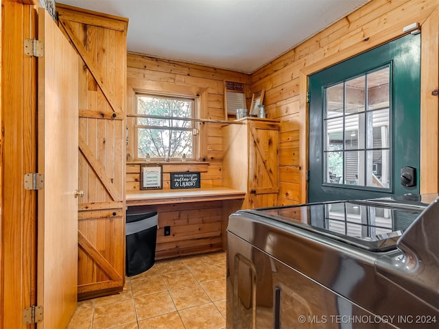 kitchen with brown cabinets, wooden walls, washer and clothes dryer, and light tile patterned floors