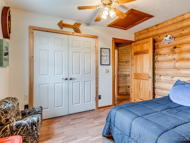 bedroom featuring attic access, light wood-style flooring, ceiling fan, log walls, and a closet