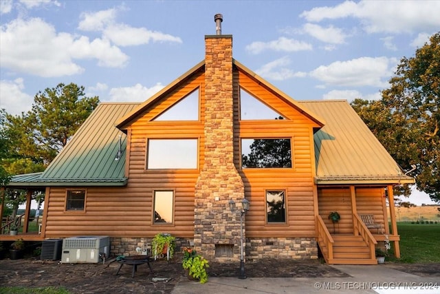 rear view of house featuring central air condition unit, faux log siding, a chimney, and metal roof