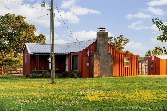 exterior space featuring metal roof, fence, a yard, board and batten siding, and a chimney