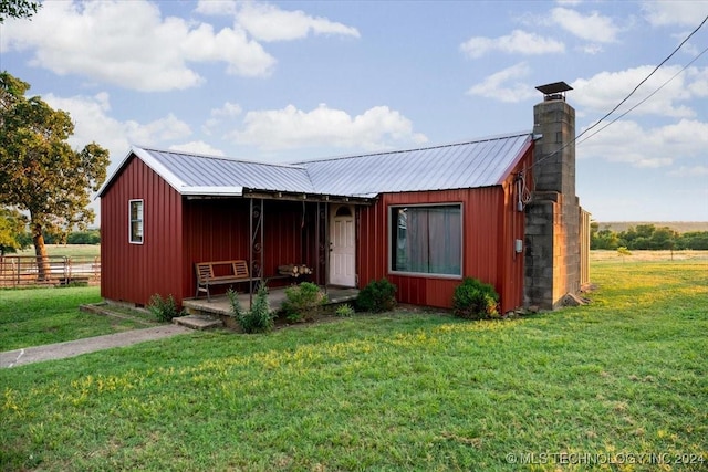 view of front facade with a chimney, board and batten siding, a front yard, metal roof, and fence