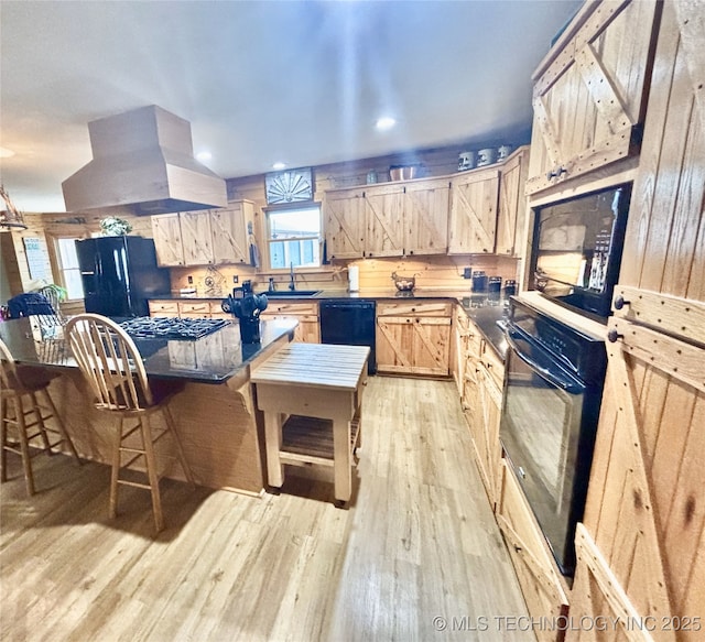 kitchen with island range hood, a sink, light wood-style floors, light brown cabinetry, and black appliances