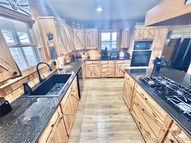 kitchen featuring light wood-style flooring, light brown cabinets, a sink, dark stone countertops, and black appliances