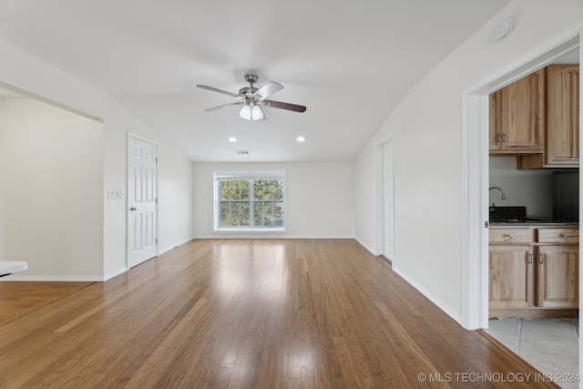 unfurnished living room featuring light hardwood / wood-style flooring, sink, vaulted ceiling, and ceiling fan