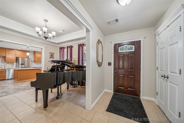 foyer entrance featuring light tile patterned flooring, ornamental molding, and an inviting chandelier