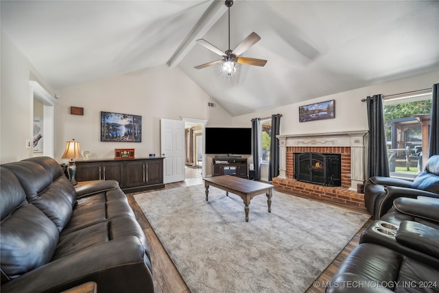 living room featuring ceiling fan, wood-type flooring, beamed ceiling, and a brick fireplace