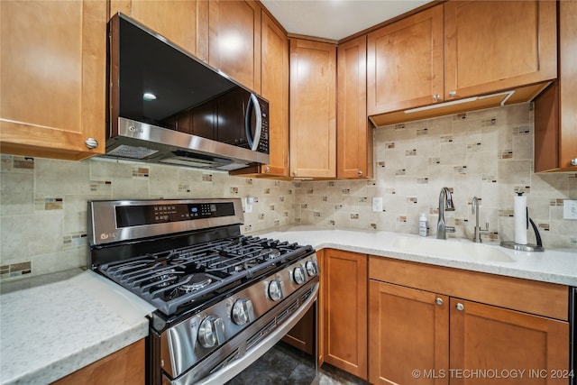 kitchen with light stone countertops, appliances with stainless steel finishes, sink, and decorative backsplash