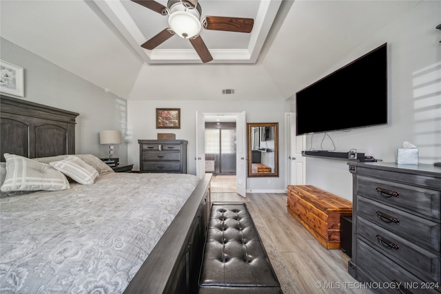 bedroom with ceiling fan, vaulted ceiling, a tray ceiling, and light wood-type flooring