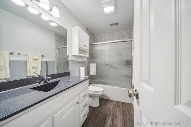 full bathroom featuring vanity, hardwood / wood-style floors, bath / shower combo with glass door, and toilet