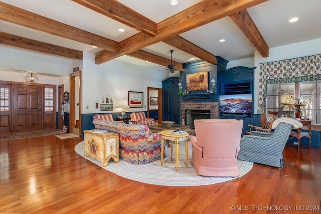 living room with a healthy amount of sunlight, hardwood / wood-style flooring, beamed ceiling, and a brick fireplace