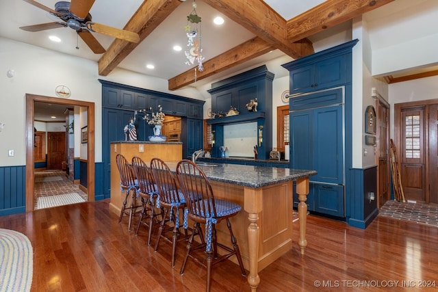 kitchen featuring sink, beamed ceiling, dark wood-type flooring, blue cabinetry, and a breakfast bar area