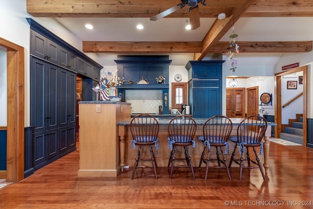 kitchen with ceiling fan, a kitchen breakfast bar, hardwood / wood-style flooring, blue cabinetry, and beamed ceiling