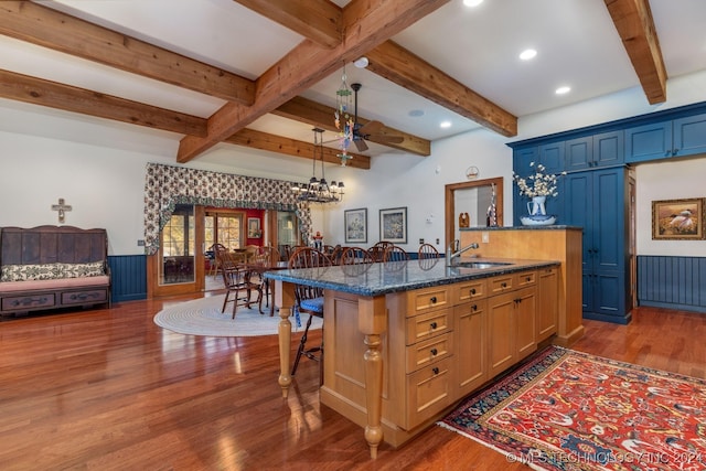 kitchen with an island with sink, an inviting chandelier, a breakfast bar, dark hardwood / wood-style floors, and sink