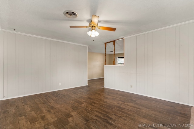 spare room featuring wood walls, a textured ceiling, ceiling fan, ornamental molding, and dark hardwood / wood-style floors