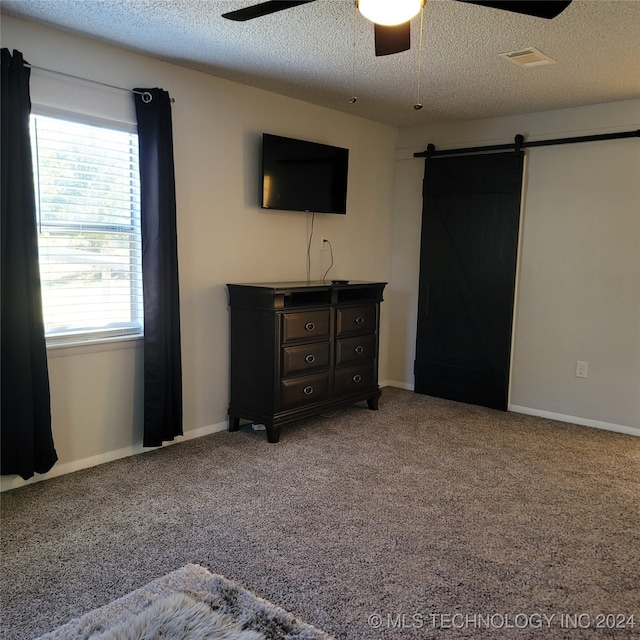 unfurnished bedroom featuring carpet, a barn door, a textured ceiling, and ceiling fan