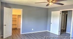 unfurnished bedroom featuring a closet, a spacious closet, dark wood-type flooring, and ceiling fan