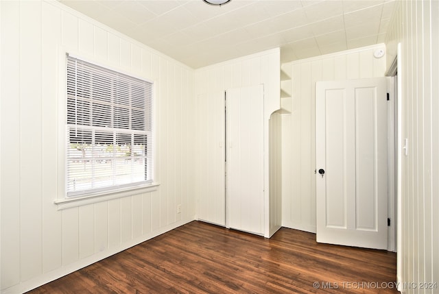 unfurnished bedroom with a closet, ornamental molding, wooden walls, and dark hardwood / wood-style floors