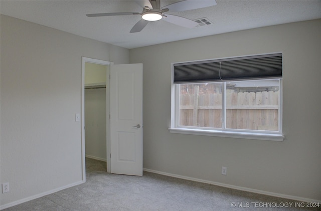 unfurnished bedroom with a spacious closet, light colored carpet, ceiling fan, and a closet