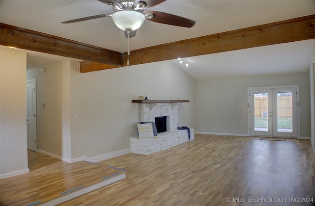 unfurnished living room with a stone fireplace, lofted ceiling with beams, a textured ceiling, light wood-type flooring, and ceiling fan