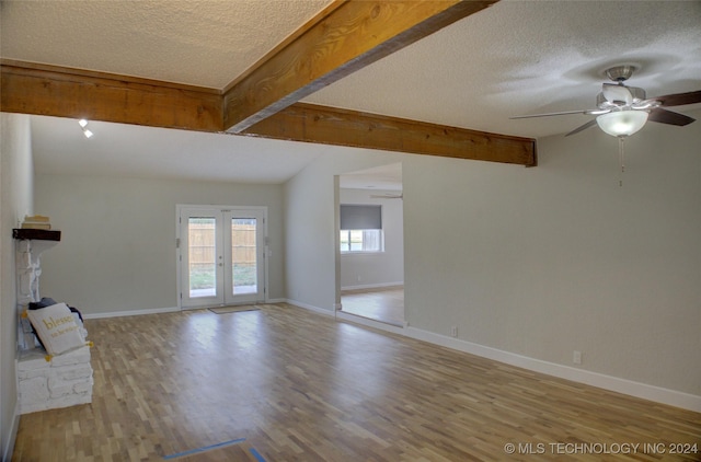 unfurnished living room featuring vaulted ceiling with beams, light wood-type flooring, ceiling fan, a textured ceiling, and french doors