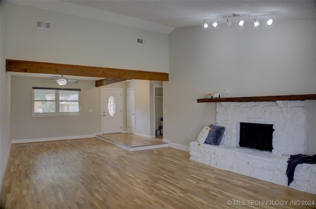 unfurnished living room featuring lofted ceiling, a stone fireplace, a textured ceiling, ceiling fan, and hardwood / wood-style floors