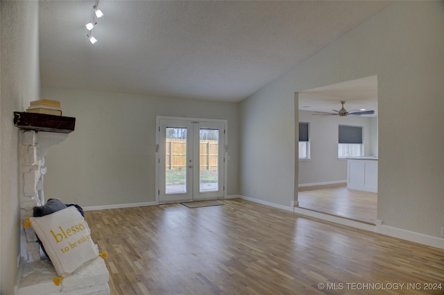 unfurnished living room featuring french doors, vaulted ceiling, a textured ceiling, and light wood-type flooring