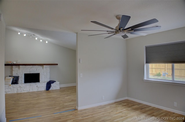 unfurnished living room featuring ceiling fan, a fireplace, vaulted ceiling, and light wood-type flooring