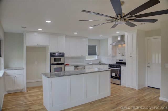 kitchen featuring white cabinetry, appliances with stainless steel finishes, light stone countertops, and wall chimney range hood