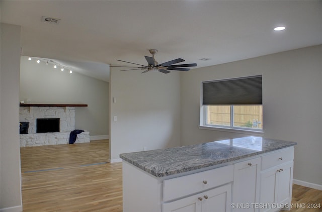 kitchen with ceiling fan, white cabinetry, light stone counters, a stone fireplace, and light wood-type flooring