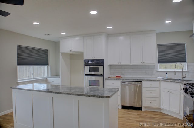 kitchen featuring appliances with stainless steel finishes, sink, white cabinets, a center island, and light stone countertops