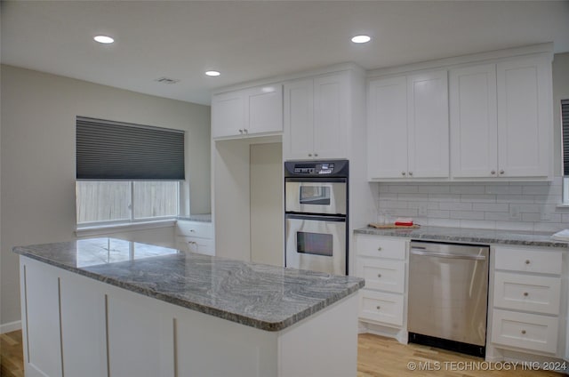 kitchen with white cabinetry, stainless steel appliances, light stone counters, light hardwood / wood-style floors, and a kitchen island