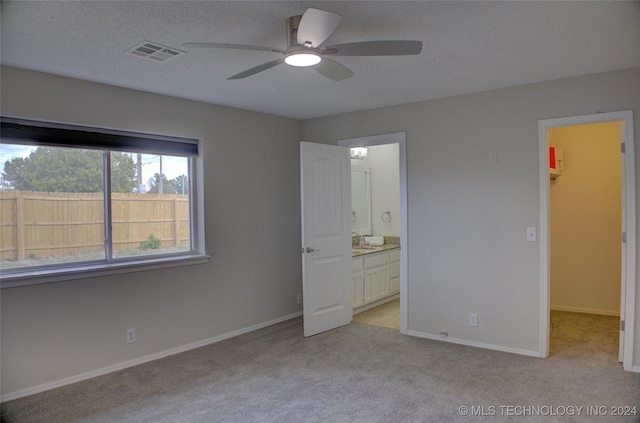 unfurnished bedroom featuring ensuite bathroom, sink, a spacious closet, ceiling fan, and light carpet