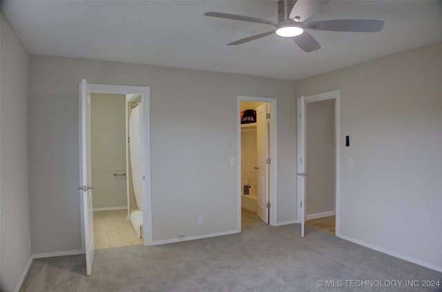 unfurnished bedroom featuring ceiling fan, ensuite bathroom, a spacious closet, and light colored carpet