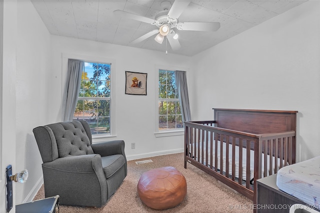 carpeted bedroom featuring ceiling fan and a nursery area