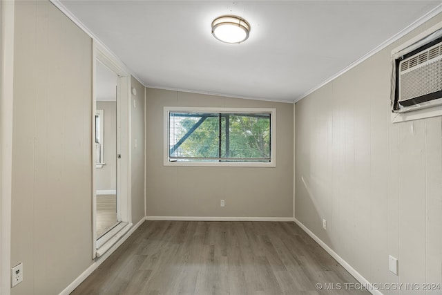 spare room with ornamental molding, wooden walls, vaulted ceiling, and hardwood / wood-style flooring