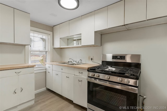 kitchen with white cabinetry, sink, stainless steel gas stove, and light wood-type flooring