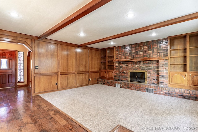 unfurnished living room featuring wood walls, beamed ceiling, a textured ceiling, and dark hardwood / wood-style flooring