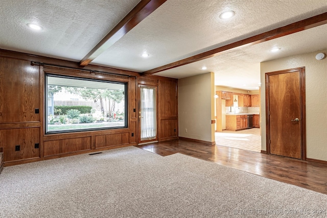 interior space with light hardwood / wood-style flooring, a textured ceiling, beamed ceiling, and wood walls