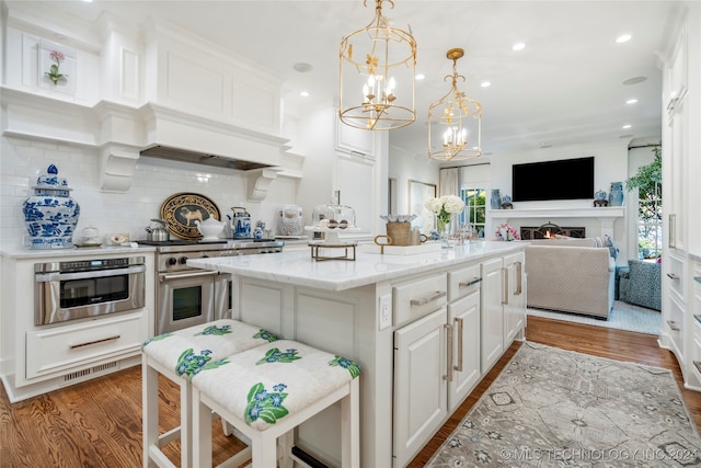 kitchen with a kitchen island, hardwood / wood-style flooring, stainless steel appliances, a kitchen bar, and white cabinetry