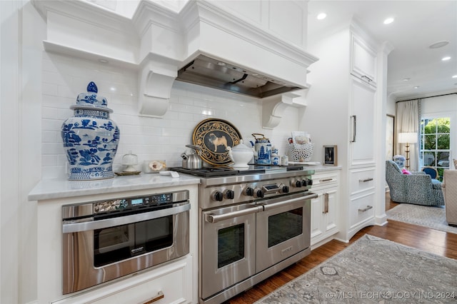 kitchen featuring stainless steel appliances, white cabinets, dark wood-type flooring, decorative backsplash, and premium range hood