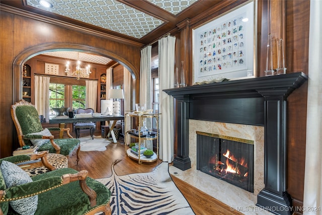 living room featuring light wood-type flooring, a premium fireplace, wooden walls, ornamental molding, and a chandelier