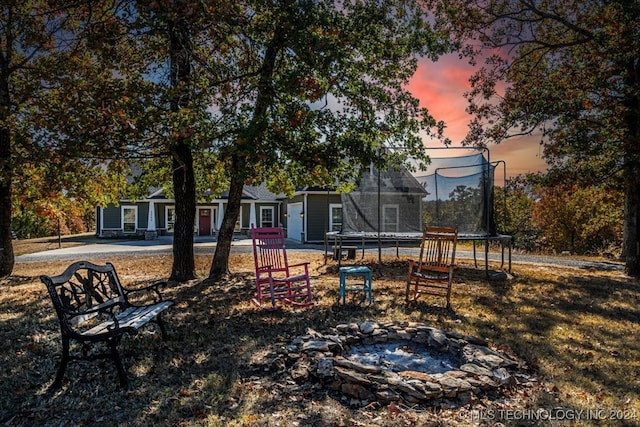 yard at dusk with an outdoor fire pit, a patio, and a trampoline