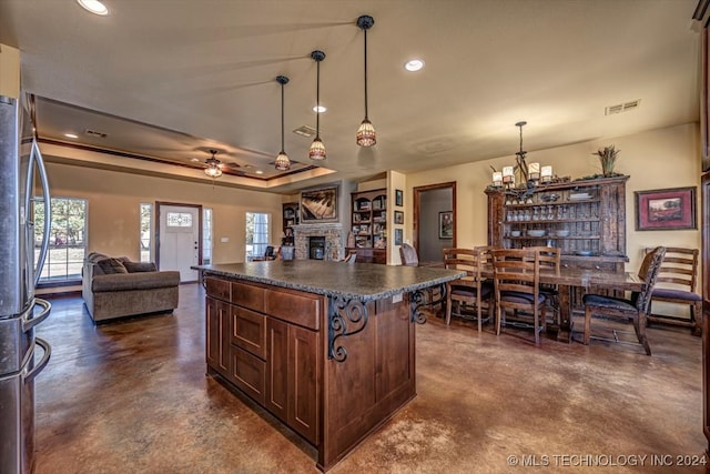 kitchen with ceiling fan with notable chandelier, a kitchen island, a fireplace, decorative light fixtures, and stainless steel refrigerator