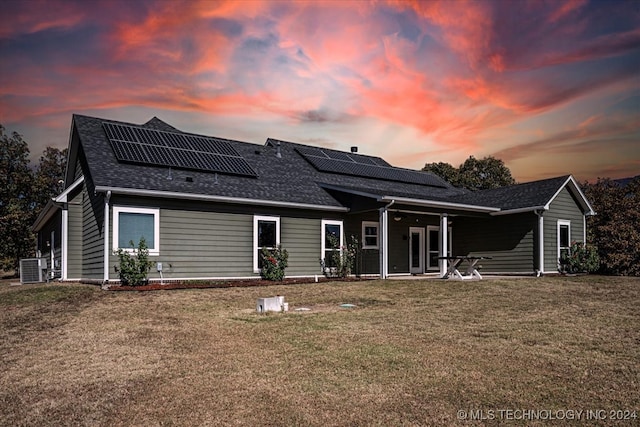 back house at dusk with a patio area, solar panels, and a lawn