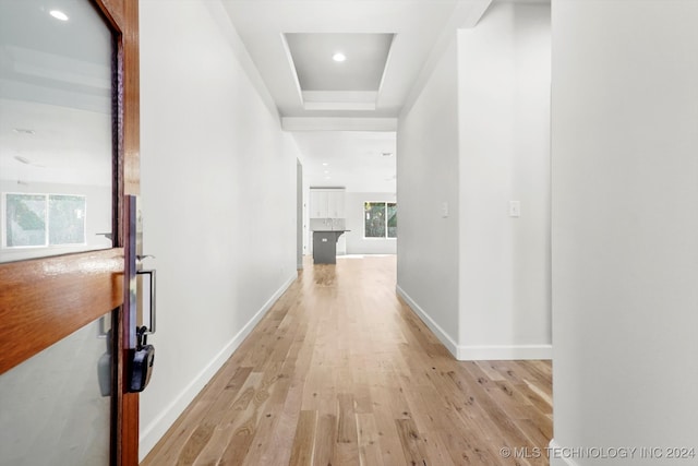 hall featuring light wood-type flooring and a raised ceiling