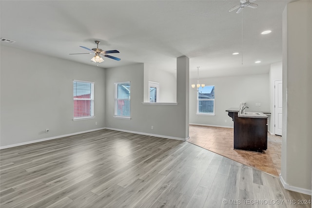 unfurnished living room featuring sink, ceiling fan with notable chandelier, and light hardwood / wood-style floors