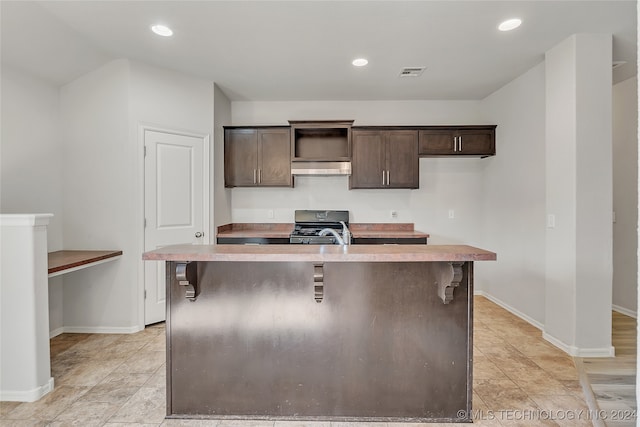 kitchen featuring a kitchen island with sink, extractor fan, range with gas stovetop, a kitchen breakfast bar, and dark brown cabinets