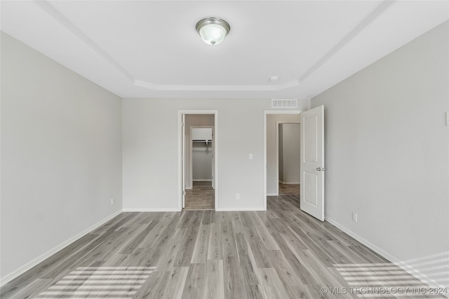 unfurnished bedroom featuring a closet, a tray ceiling, light wood-type flooring, and a walk in closet